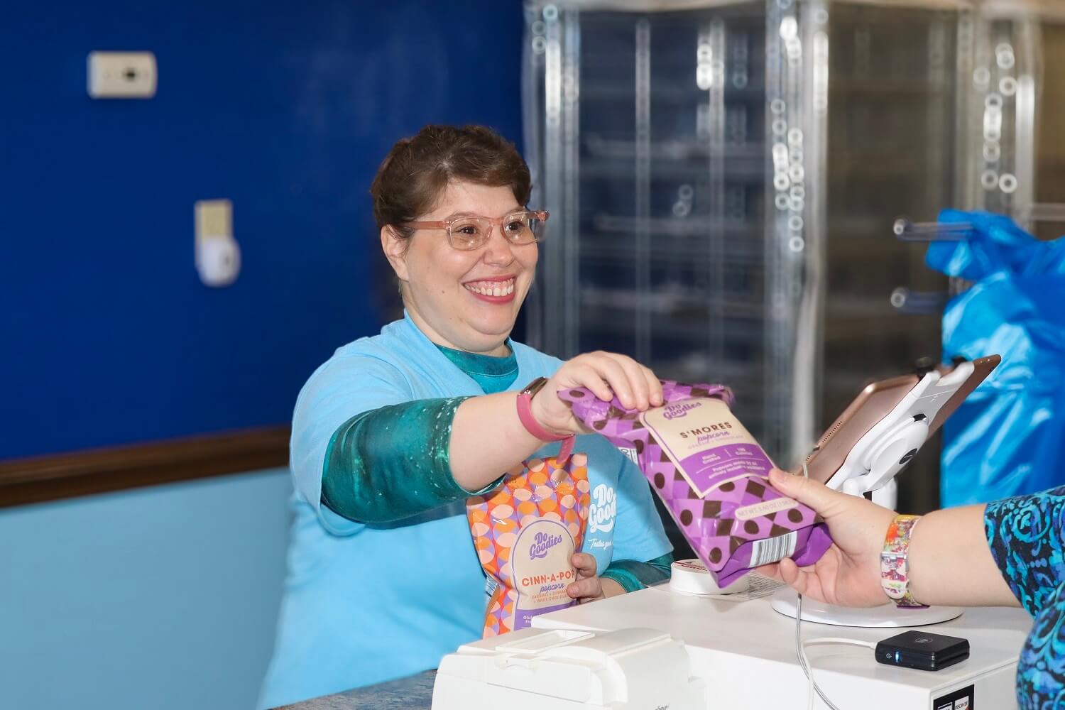 A Do Goodies employee selling a packet of smores popcorn with a huge smile on her face